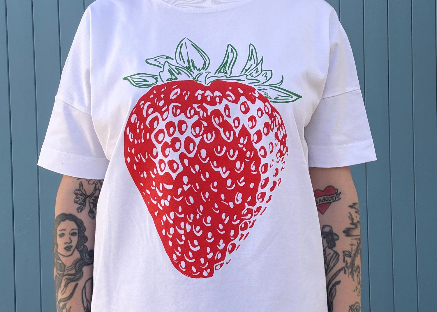 Person wearing a white t-shirt with a red strawberry graphic on a blue wooden floor.