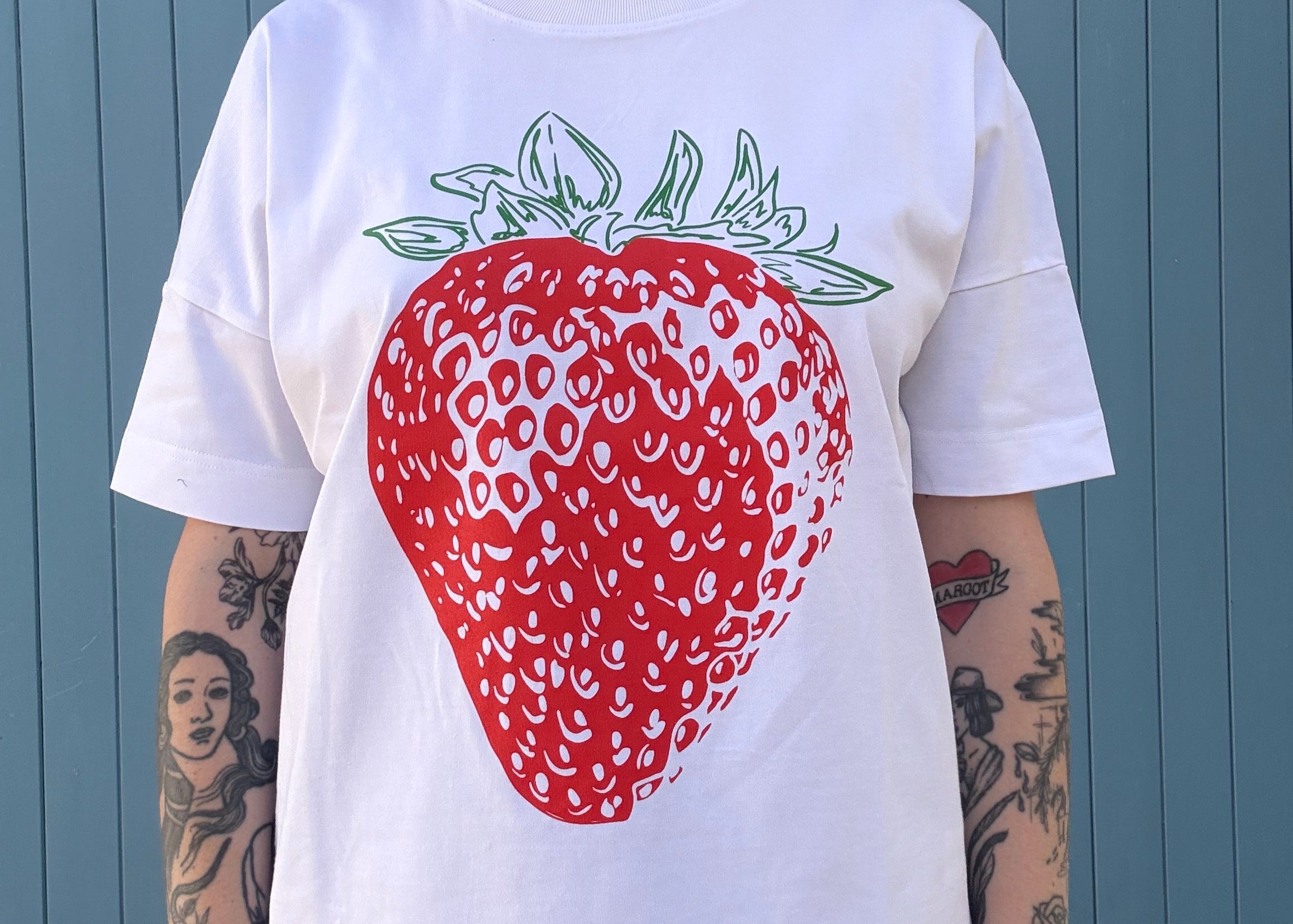 Person wearing a white t-shirt with a red strawberry graphic on a blue wooden floor.